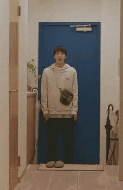 a man in a white hoodie is standing in front of a blue door .