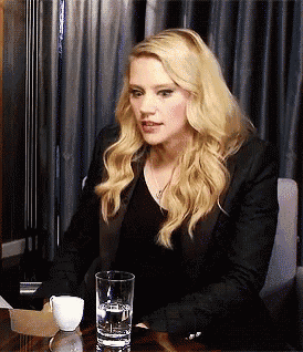 a woman sits at a table with a glass of water and a cup of coffee