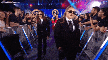 two women in suits and sunglasses are walking through a crowd at a concert .