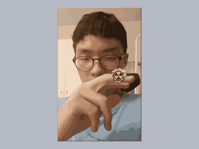 a young man wearing glasses holds a skull and crossbones ring