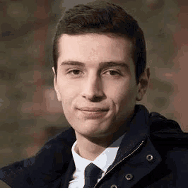 a young man wearing a jacket and tie is smiling at the camera .