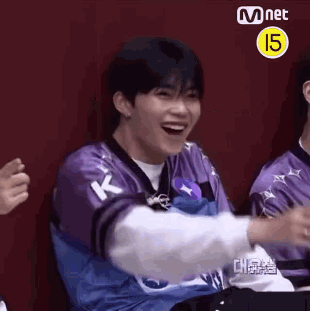 a man in a purple shirt is laughing while sitting next to another man .
