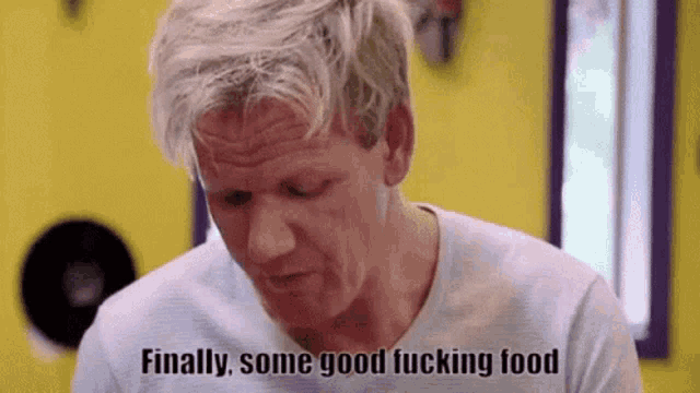 a man is sitting at a table with a yellow background and says `` finally some good fucking food '' .