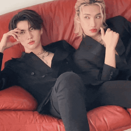 two men are sitting on a red couch wearing black suits .