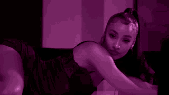 a woman in lingerie is laying on her stomach on the floor in a purple light .