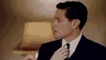 a man in a suit and tie is adjusting his tie while standing next to a lamp .