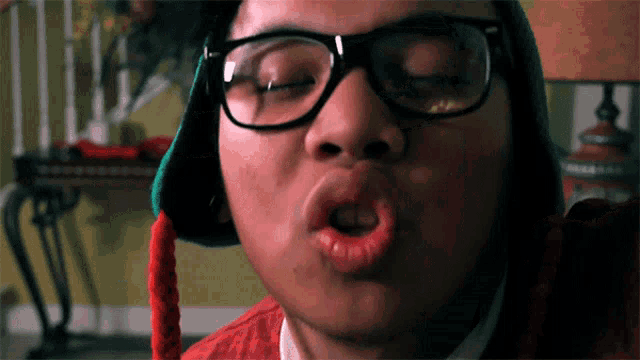 a young man wearing glasses and a hat makes a funny face