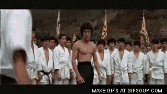 a man without a shirt is standing in front of a group of karate fighters .