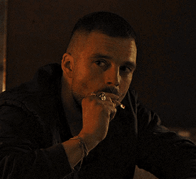 a man with a ring on his finger is smoking a cigarette in a dark room