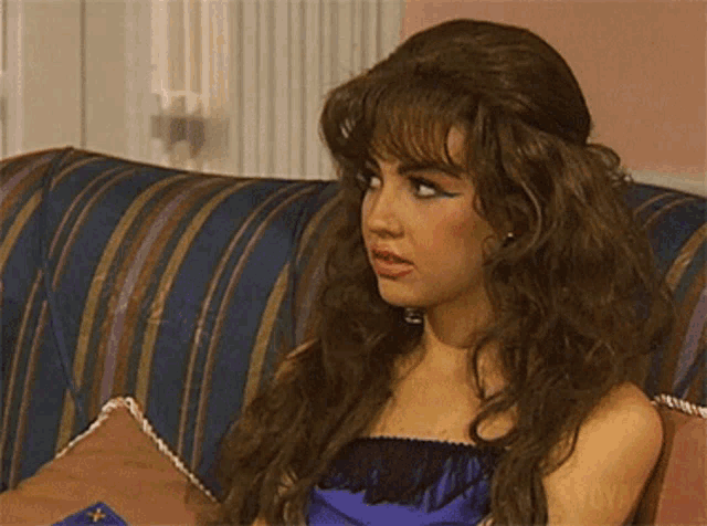 a woman with long hair is sitting on a striped couch and looking at the camera