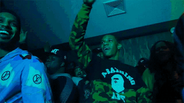 a man wearing a green and black bape shirt stands in a crowd