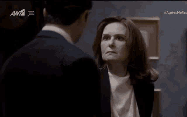 a man in a suit and a woman in a white shirt are looking at each other in a dark room .