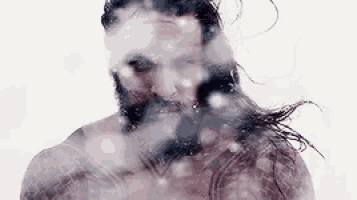 a shirtless man with a beard is taking a shower with water coming out of his face .