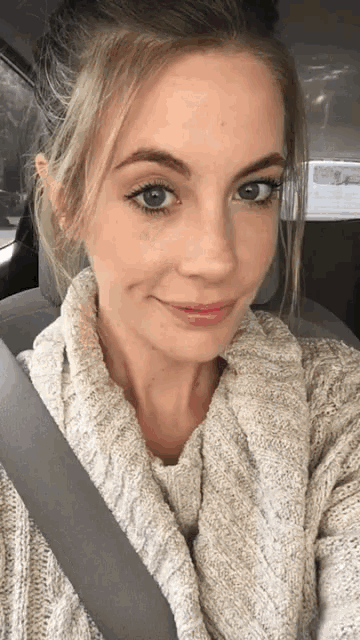 a woman wearing a sweater and scarf takes a selfie in a car