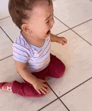 a baby is crying while sitting on the floor on his knees .