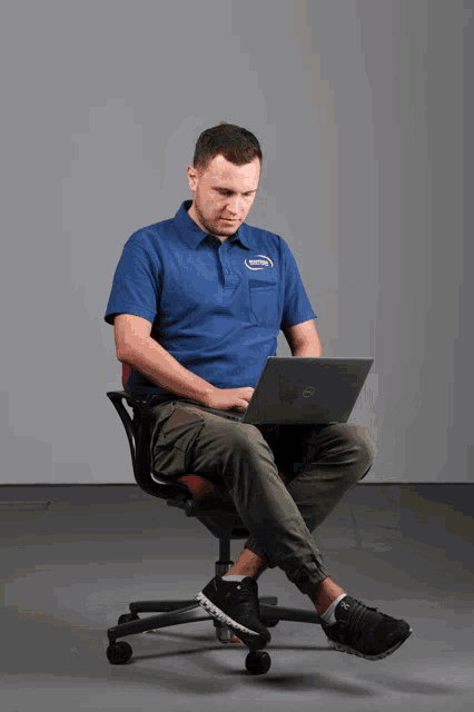 a man in a blue shirt is sitting in an office chair using a dell laptop computer