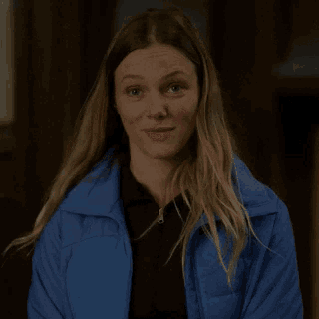 the woman is wearing a blue jacket and making a funny face .