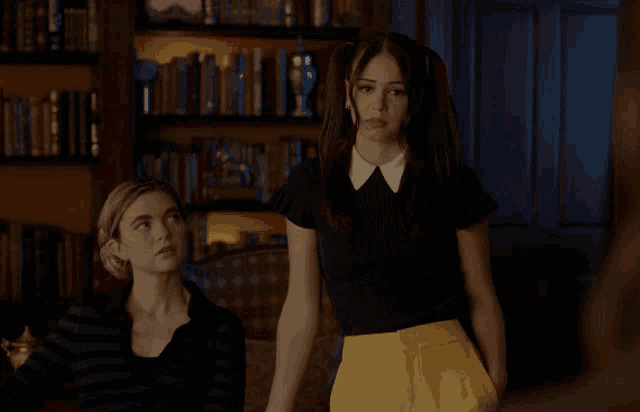 two women standing next to each other in front of a bookcase