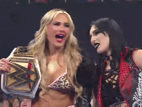 two women are standing next to each other with one holding a wrestling belt
