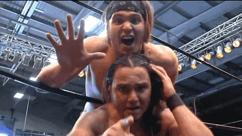 a wrestler with a bandana on his head holds another wrestler 's head