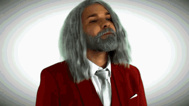 a man with long gray hair and a beard is wearing a red suit and tie