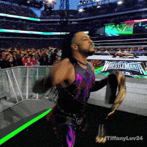 a wrestler is holding a championship belt in front of a sign that says wrestlemania on it
