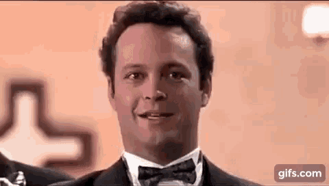 a man wearing a tuxedo and bow tie is smiling .