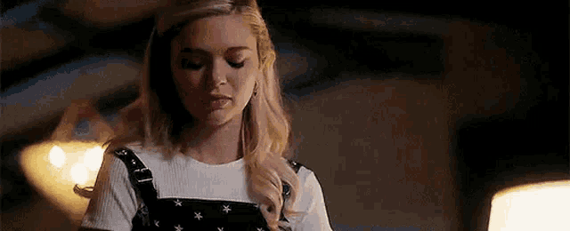 a woman is standing in a dark room wearing overalls and a white top .