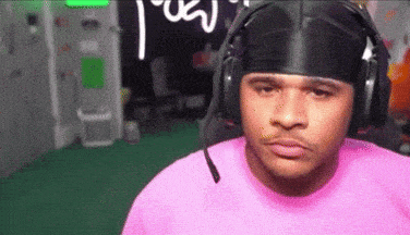 a man wearing headphones and a pink shirt is making a face .