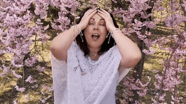 a woman in a white shawl is standing in front of a tree with pink flowers .