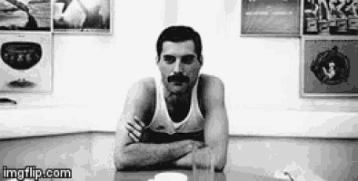 a black and white photo of a man with a mustache sitting at a table .