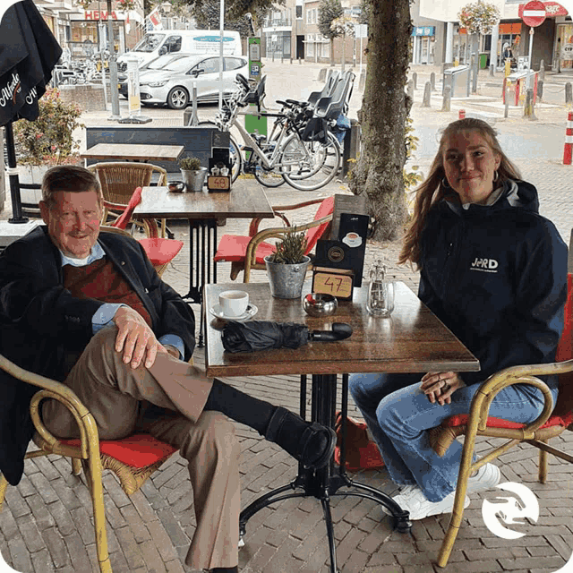 a man and a woman sit at a table with the man wearing a jacket that says jrd