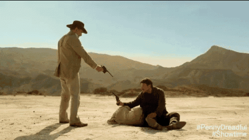 a man is pointing a gun at another man laying on the ground in the desert