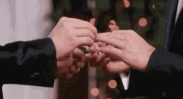 two men are putting rings on each other 's fingers .
