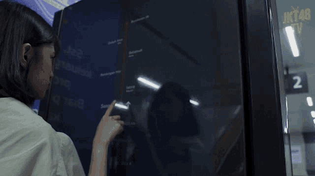 a woman is pointing at a screen that says jkt48 on it