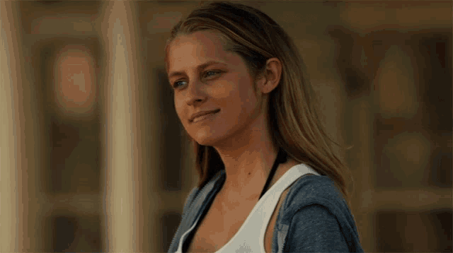 a woman wearing a white tank top and a blue sweater smiles