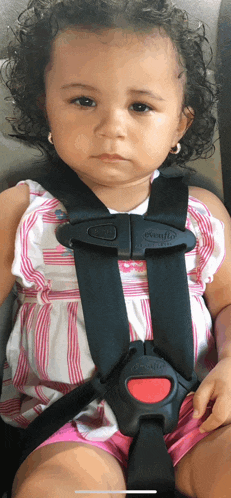 a little girl wearing a pink and white striped dress is sitting in a car seat