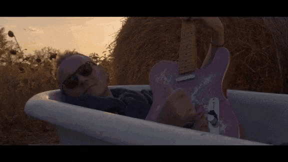 a man in a bathtub with a pink guitar