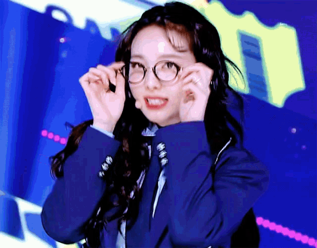 a young woman wearing glasses and a blue jacket is making a funny face .