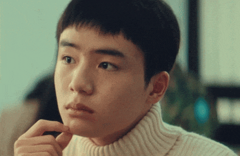 a young man wearing a white turtleneck sweater looks at something