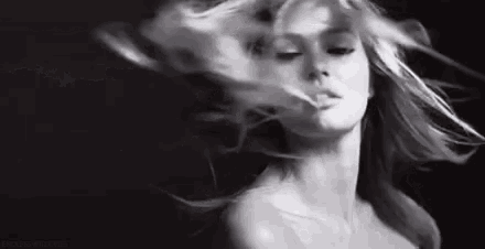 it is a black and white photo of a woman with long hair blowing in the wind .