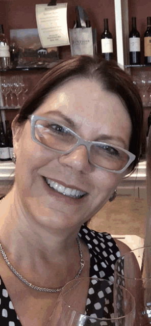 a woman wearing glasses is smiling and holding a glass