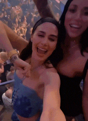 two women are taking a selfie in front of a crowd and one has a tattoo on her arm that says cnv