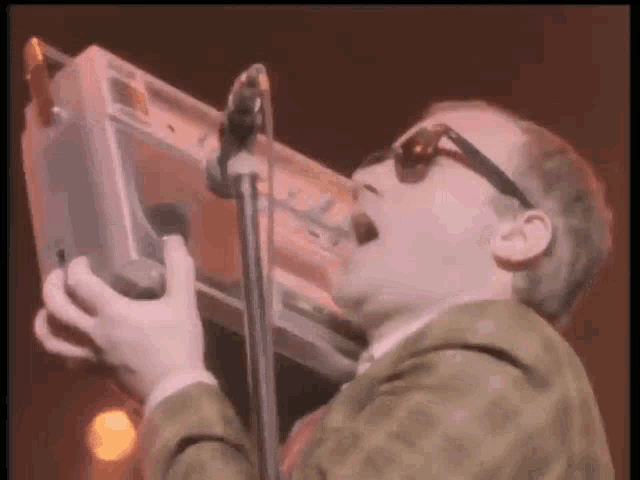 a man wearing sunglasses is singing into a microphone while playing a keyboard
