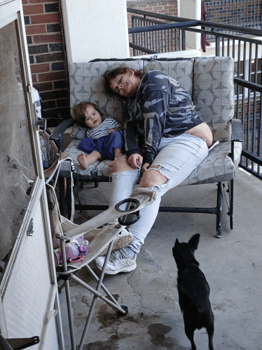 a woman sits on a couch with a child and a dog looking on