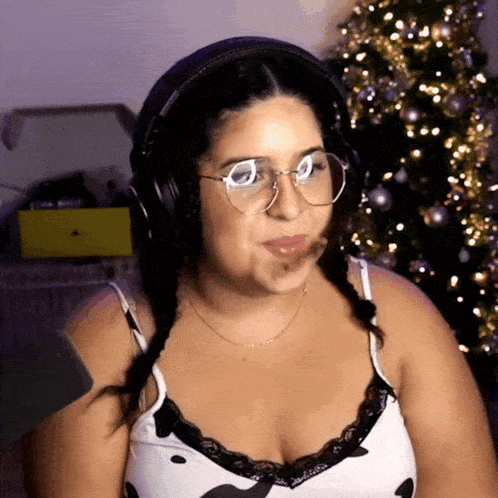 a woman wearing headphones and glasses looks at the camera in front of a christmas tree
