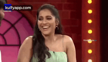 a woman in a green dress is laughing on a stage in front of a red wall .