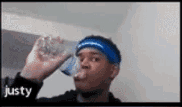 a man wearing a blue headband is drinking a glass of water .