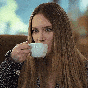 a woman is drinking a cup of coffee in a cafe