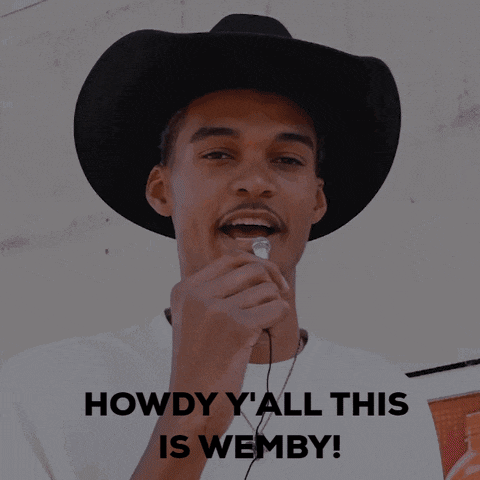a man wearing a cowboy hat is holding a microphone with the words howdy y'all this is wemby behind him
